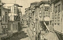 A narrow street, with tall buildings with balconies on either side