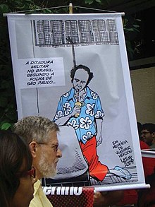 Protest against the usage of the term. The banner, a cartoon by Carlos Latuff, sarcastically adds a glass and straw to the famous photo of Vladimir Herzog hanged after torture, with the implication that the Folha de S.Paulo is trying to whitewash the realities of the dictatorship that killed him in 1975. It says: "The military dictatorship in Brazil according to Folha de S.Paulo". Vlado Herzog protest.jpg