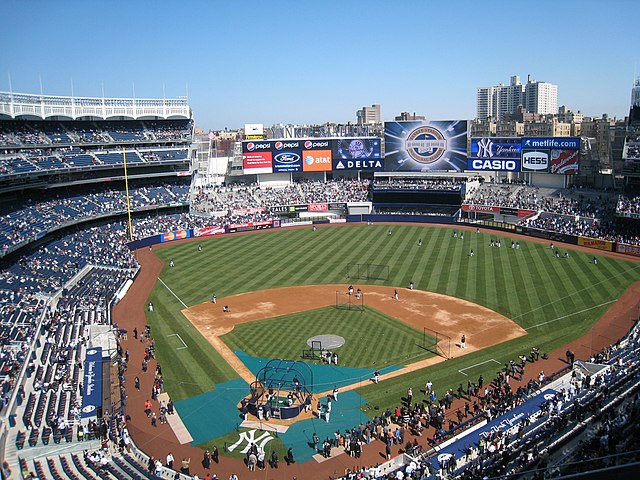 A baseball stadium with blue seats and buildings visible in the background.