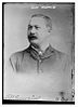 A black-and-white photograph of a man with a curling mustache