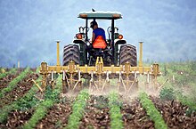 A tractor pulling a tiller Farmer and tractor tilling soil.jpg