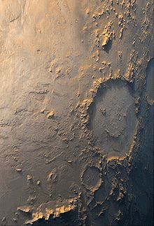 Zdjęcie. Oświetlony z boku krater uderzeniowy, z wzniesieniami przypominającymi piktogram uśmiechniętej twarzy.