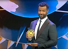 Host Isaiah Mustafa with the current LMGI award in 2021 Isaiah with award.jpg