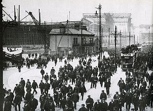 Workers leaving the Harland & Wolff shipyard in early 1911. The RMS Titanic can be seen in the background, underneath the Arrol Gantry. Knocking off at Harland & Wolff, Belfast.jpg