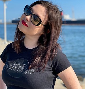 A white woman with brown hair is wearing a black t-shirt (that reads "dark universe"); she is wearing sunglasses, looking and facing the camera's left.