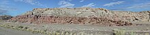 The Jurassic-Cretaceous boundary is seen where the red and purple beds of the Morrison Formation abruptly contact the drab, gray bed of the overlying Cedar Mountain Formation. The contact is the K1 unconformity. Jessie's Twist, southwest of Green River City, Utah. Morrison-Cedar Mountain Formations.jpg