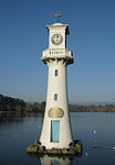 Minature white lighthouse in lake with a small model of a sailing ship on top