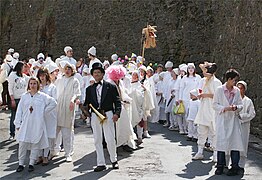 Un homme à lunettes, habillé d'un haut-de-forme et d'une queue-de-pie, dirige un cortège de Soufflaculs, tous vêtus de chemises de nuit blanches et de bonnets de coton blanc, avec à leurs mains des soufflets.