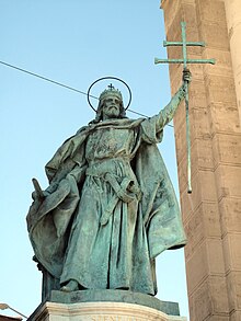 Photo d'une statue en bronze d'un homme barbu portant un couronne et une auréole et qui lève du bras une croix