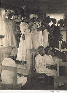 African-Americans in church during a church service. Black churches served soul food meals to the feed the African-American community. Ulmann, African-American Church.jpg