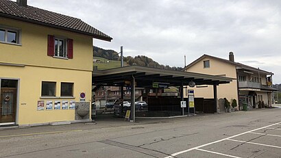 Two-story station building with gabled roof next to canopy-covered waiting area