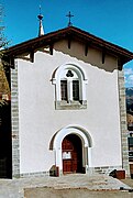 Photographie d'une église blanche avec ses portes ; les vitraux sont gothiques et dominent la porte.