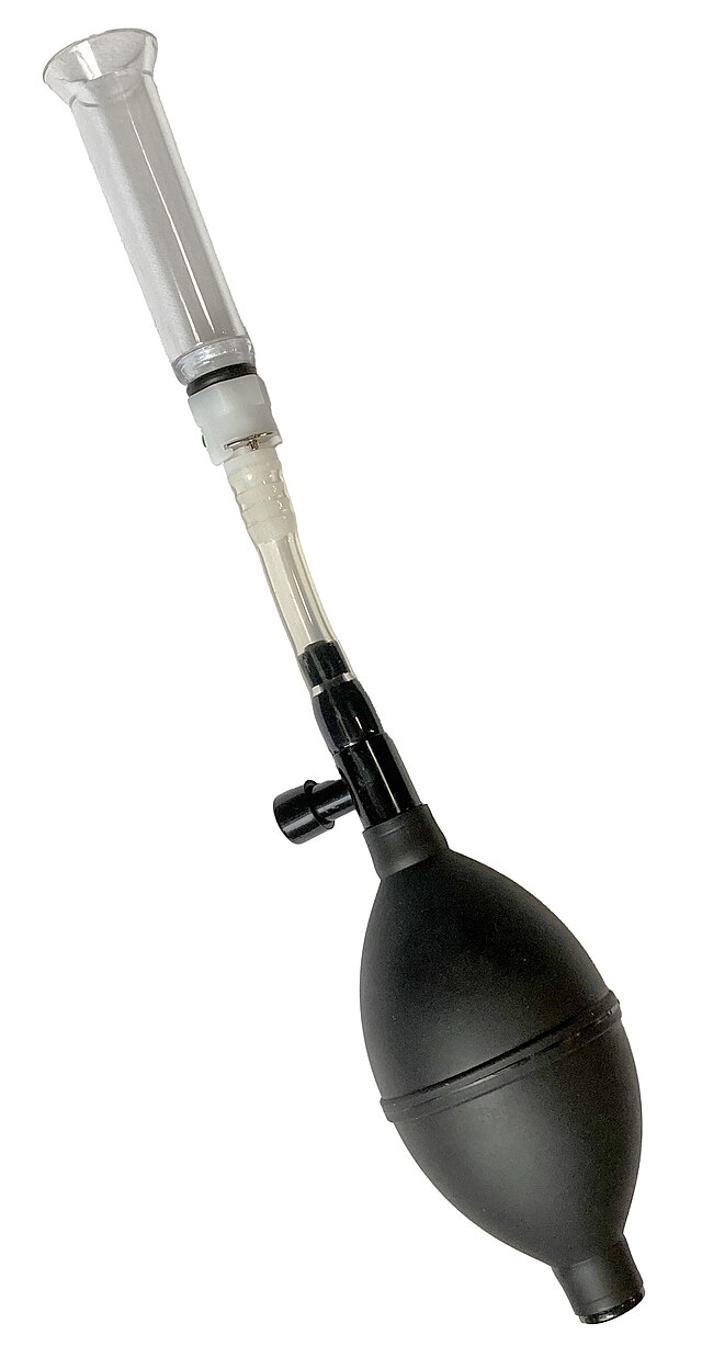 There are multiple parts of this object. At the top (of the image) is the clear acrylic cylinder, which screws onto the rest of the device. There is a tube in the center, connected to a larger bulb that can be squeezed to add air. The black knob on the side is the release valve, which depressurizes the air when pressed.