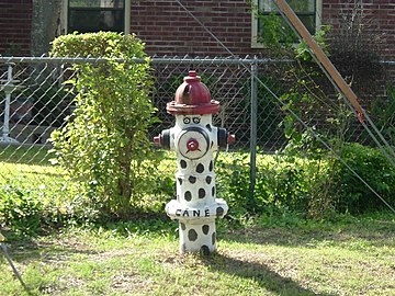 ein weiß gestrichener Hydrant mit schwarzen Tupfen mit Gesicht, sieht aus wie ein trauriger Clown