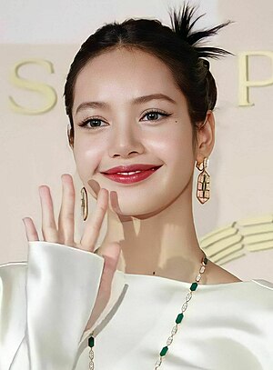 Image of Lisa smiling and waving, she is dressed in white and she is wearing jewels