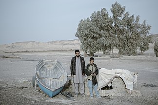 Father and son stand by the boat left in Hamun arid land.