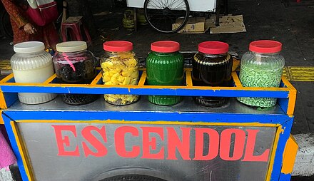 Jars of roadside es cendol ingredients on display, from left to right: coconut milk, black grass jelly, tapai, plain cendol, liquid palm sugar, and cendol in coconut milk.
