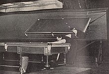 Joe Davis playing at a billiard table, with a large mirror behind him reflecting the table