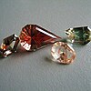 Four faceted gemstones in various cuts showing some of the Oregon labradorite colors, including dichroic red green, red and yellow bicolor, clear with copper shiller streaking, and teal blue-green.