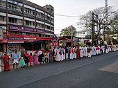 Fotografía en color de una cadena humana con adultos y niños en trajes indios en una calle.