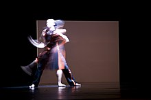 Deux personnes qui dansent, capturées en mouvement flou dans une production de ballet moderne.