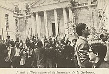 Schwarzweißfoto von Männern, die lange Holzstöcke vor der Sorbonne halten