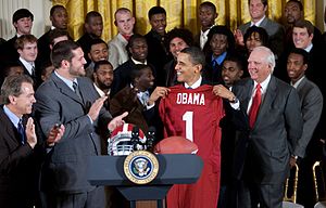 President Obama receives an Alabama jersey at the White House with various team members and coaches present.