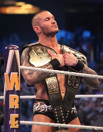 Youngest, four-time, and final champion Randy Orton, pictured here holding the Big Gold Belt (formerly representing the World Heavyweight Championship), and the 2013–2014 belt design of the WWE Championship; both belts together represented the renamed WWE World Heavyweight Championship until a single belt was introduced in August 2014.