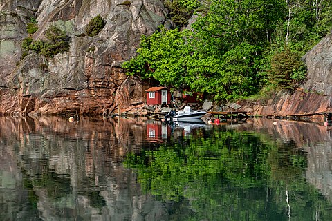 Two falu red fishing huts and a motorboat by the cliff in Rågårdsdal, Lysekil Municipality, Sweden.