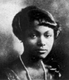 A young Black woman with hair cut in a short fringe, wearing a strand of pearls