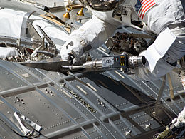 An astronaut uses a screwdriver to activate a docking port on an ISS module.