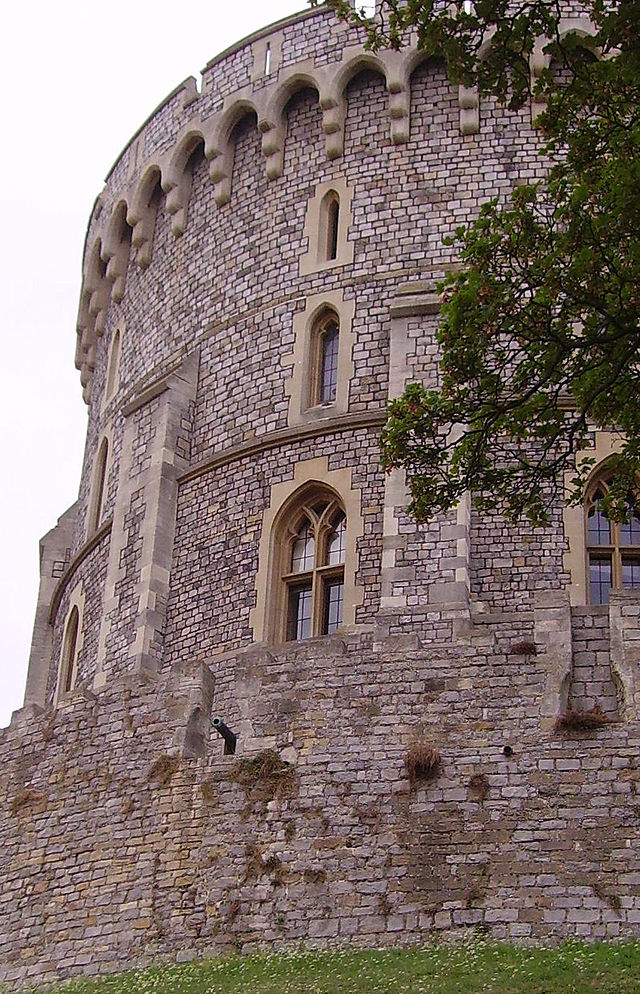 A photograph showing the left hand side of a circular stone tower made of grey stone and with small windows.