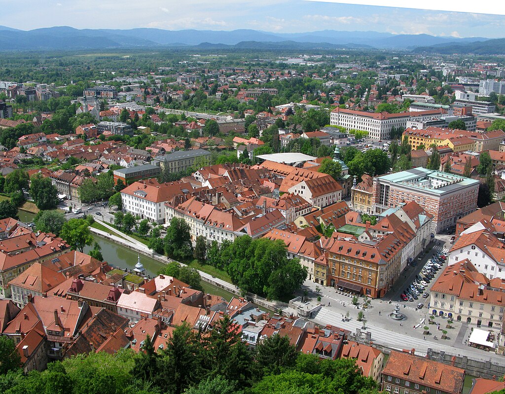 Laibach / Ljubljana. Blick von der Burg von Laibach südwestwärts: Im Vordergrund der Laibach mit der Promenade (= Blaues Band). Rechts am Bildrand die Nationalbibliothek (4-Flügelbau mit Flachdach) am Grünen Band: die Baumreihe, die an der doppeltürmigen Trnovo-Kirche (linker Bildrand) endet (UNESCO-Welterbe in Slowenien)