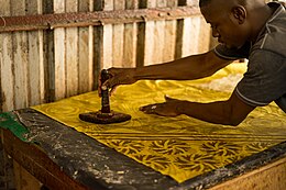 Africain penché sur un tissus et tenant un pochoir servant à l'impression des motifs