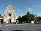 Fotografía en color de una iglesia con campanario de piedra y la plaza adyacente.