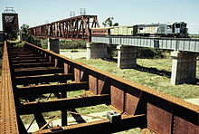 QR loco 1501 hauls a special train across the 1960s era Burdekin River bridge, September 1989. The original 1882, now disused bridge is in the foreground. Dia 0386.jpg