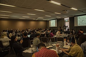 a room full of people sitting at tables watching a presentation