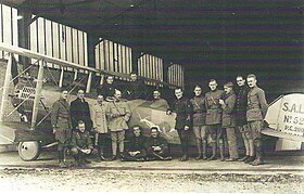 Photo noir et blanc d'un groupe d'hommes autour d'un avion biplan