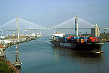 A container ship leaves the Port of Savannah after passing under the Talmadge Memorial Bridge and proceeding east down the Savannah River past the Savannah Historic District.