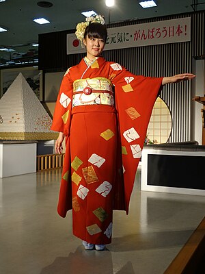 A young unmarried Japanese woman wearing a deep orange Furisode với tay áo được đưa ra ngoài.