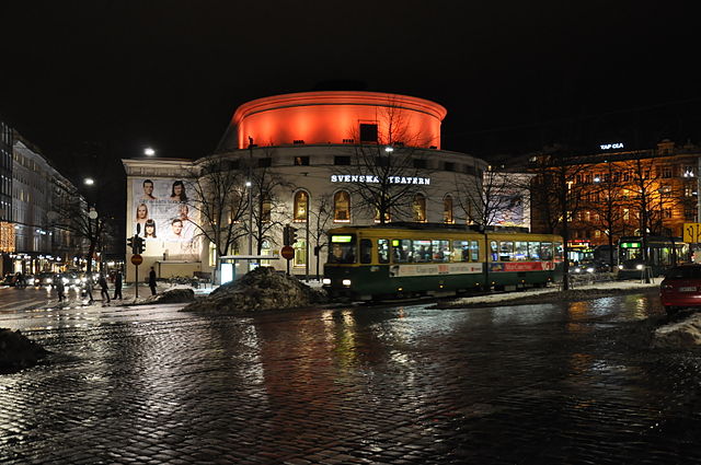 A white round building with its roof lit up orange.
