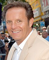 A man wearing a black jacket and a white shirt, smiling and looking away