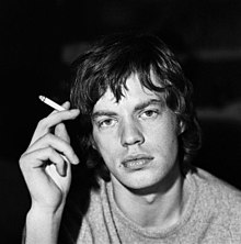 Portrait of Jagger holding a cigarette in his right hand looking directly at the camera