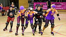 Two Wellington skaters (in purple) form a wall, limiting their opponents' movement, while their jammer (leftmost skater in purple) takes a hip whip to accelerate past the pack Roller Derby (22).jpg