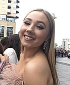 Mujer con cabello rubio sonriendo para la cámara, vistiendo un vestido rosa esponjoso