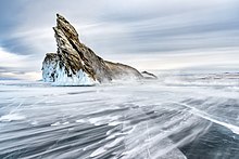 El mar helado está salpicado de ronchas heladas.  Una roca afilada se eleva hacia el cielo gris.