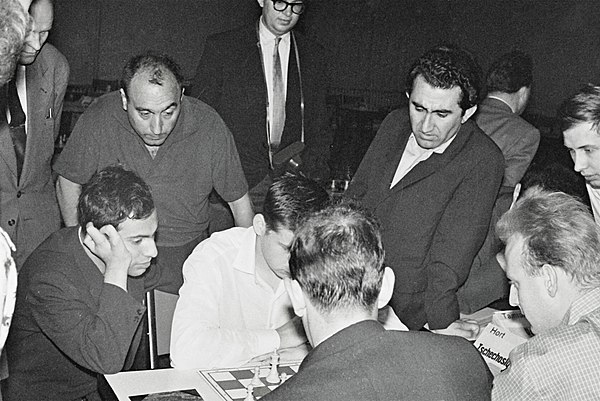 Petrosian (standing on right, with jacket) at the 1961 European Chess Team Championship. Seated, facing right, is Mikhail Tal, then world champion.