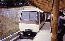 Details of the Dashaveyor's running gear are visible in this photo. The small horizontal wheels at the front steer the larger running wheels just visible behind them. The electrical supply uses a small 3rd rail shaped like a V with a pickup that pushes up on the bottom of it. The operator can also be seen in the front left of the cabin. Toronto Zoo Domain Ride enters main station.jpg