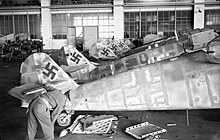 Un militare britannico esamina alcuni Bf 109 in un hangar dell'aeroporto tedesco di Wunstorf, subito dopo la cattura avvenuta l'8 aprile 1945. Gli apparecchi erano stati smontati e la vernice rimossa per un'operazione di manutenzione. Si noti la differenza tra il timone di coda della serie G-14 in primo piano e quello della serie F immediatamente dietro.