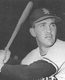 A man wearing a baseball cap and jersey poses prior to swinging his baseball bat.